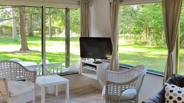 A modern living room with a TV, white wicker furniture, and a view of a green garden. - Tranquil Holiday Home in Hals near Beach (Hals)