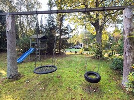 Un parque infantil con columpios y neumáticos colgantes, rodeado de árboles y césped.