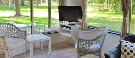 Quarto com televisão, cadeiras de vime branco, mesa branca e sofá de couro preto.