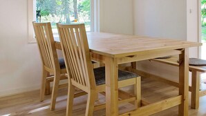A wooden dining table with four chairs, a bench, and a window with a view of trees and a swing. - Tranquil Holiday Home in Hals near Beach (Hals)