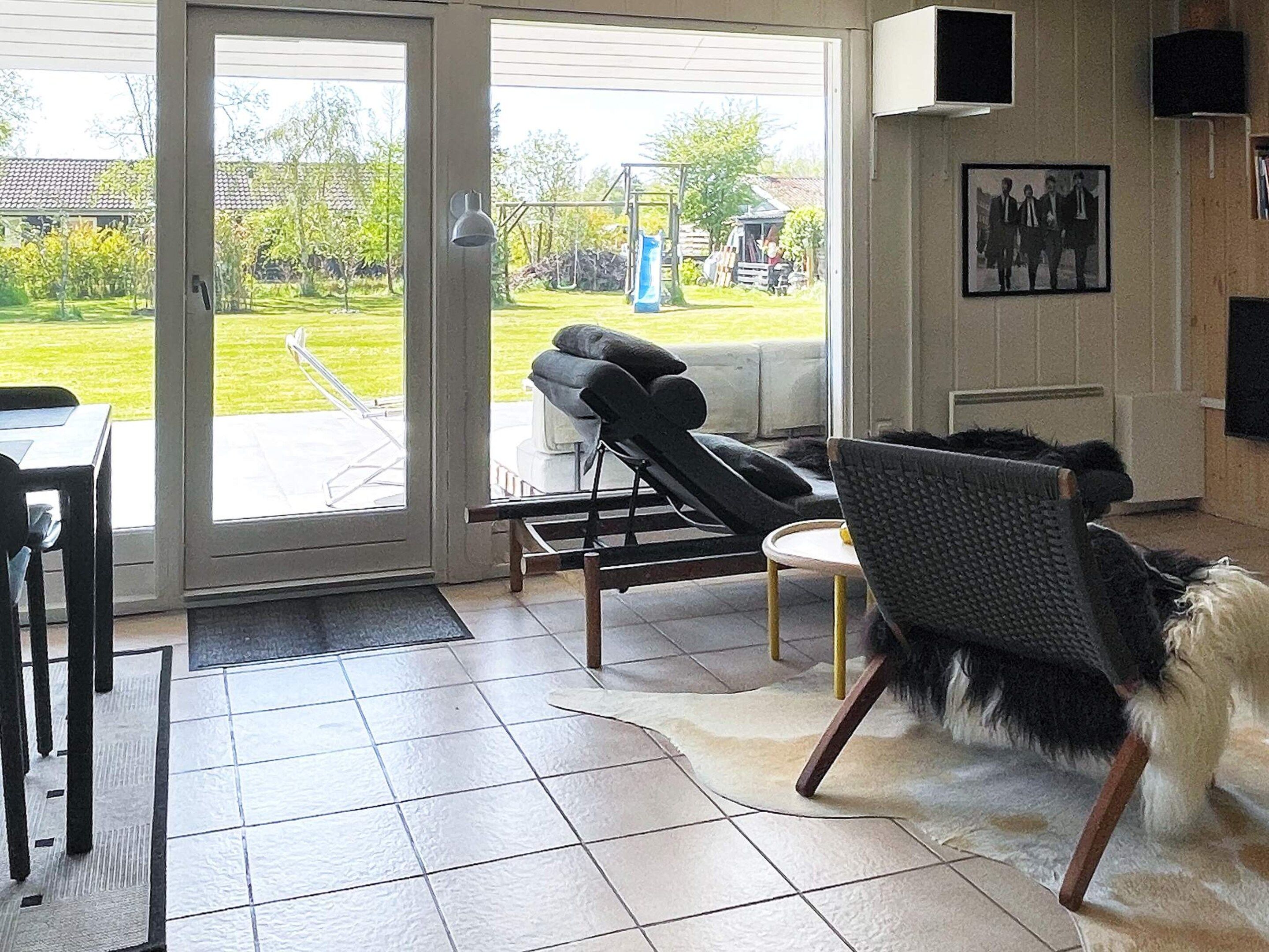 A room with a sliding glass door leading to a patio, a lounge chair, a small table, and a rug.