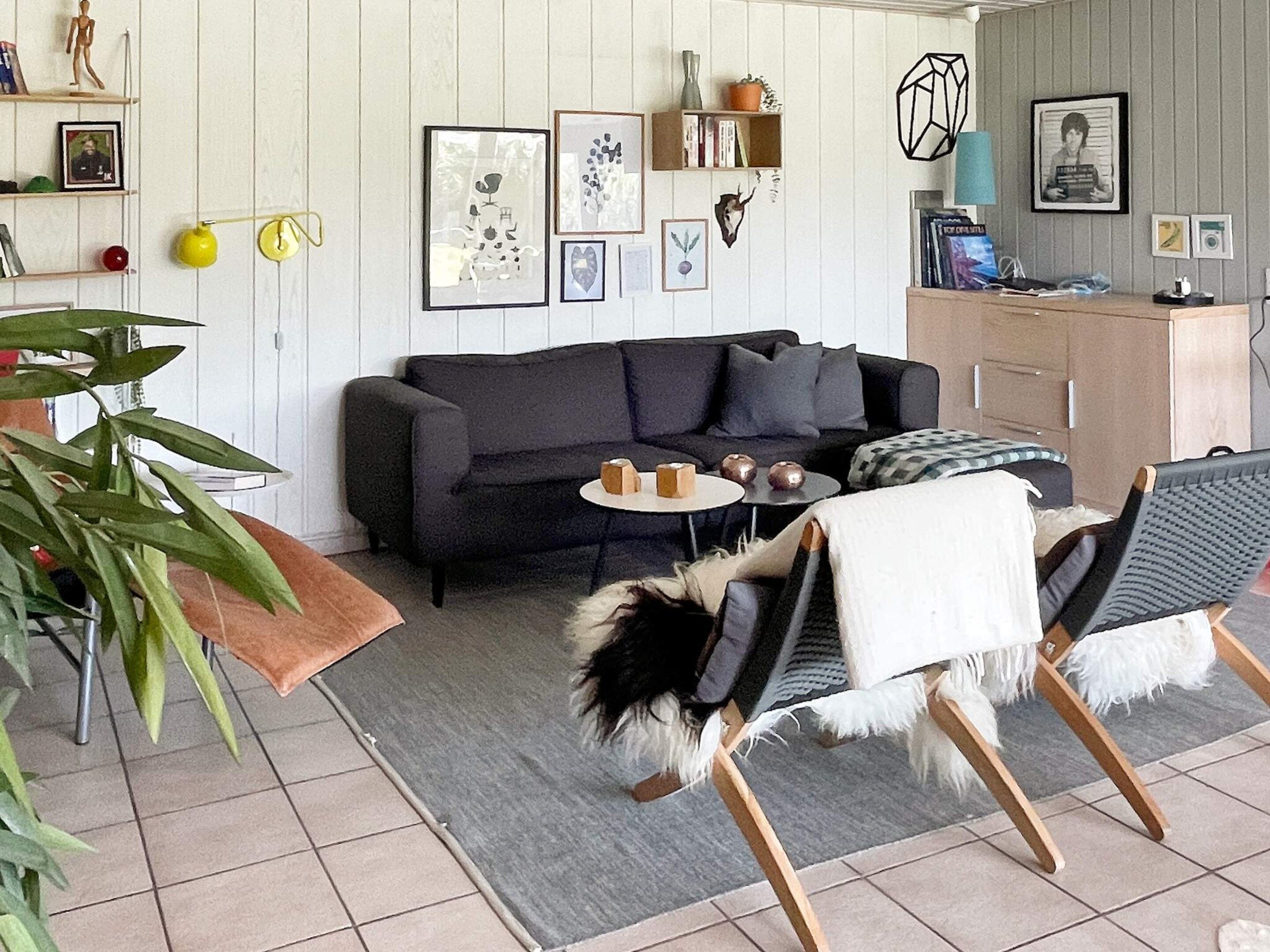 A living room with a sofa, a small round table, a dog lying on a chair, and various wall decorations.