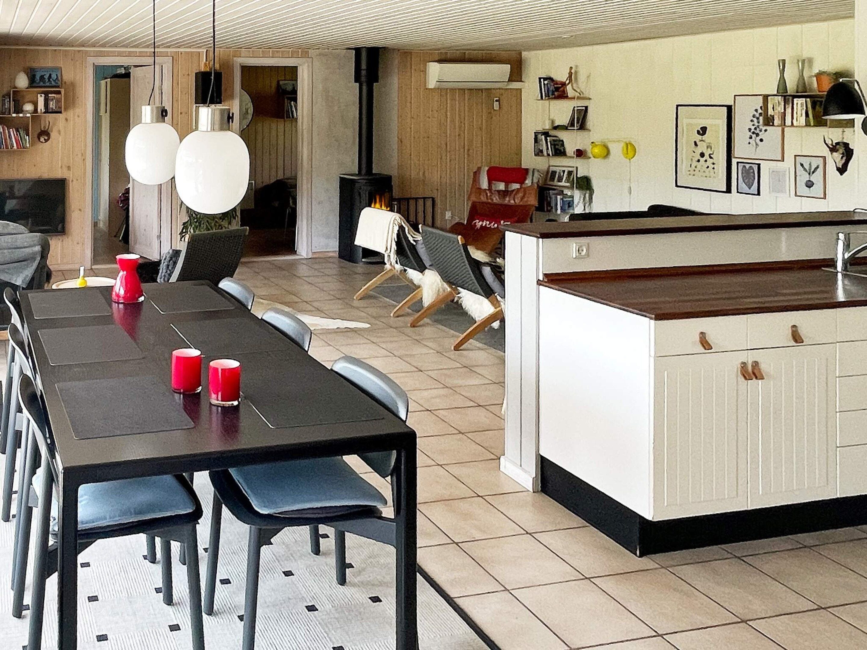A dining area with a long table, chairs, and red candles. There is a kitchen area with a stove and cabinets.