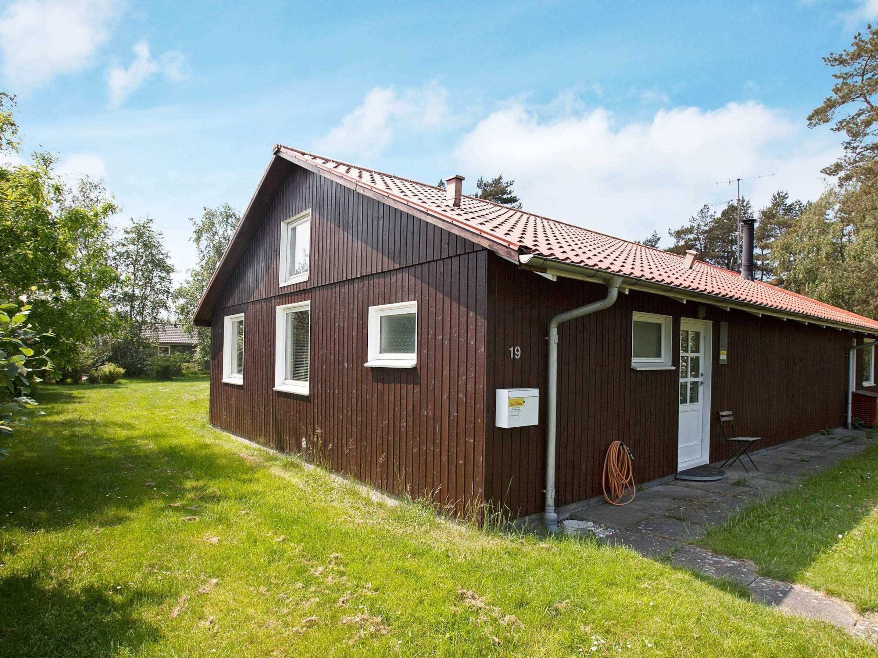 Ein einstöckiges Holzhaus mit rotem Ziegeldach, einer weißen Tür und einer kleinen Veranda.
