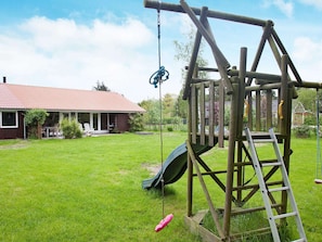 Una struttura giochi in legno con uno scivolo e altalene in un giardino sul retro.