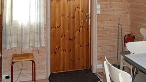 En dörr av trä med ett fönster i form av en diamant, en liten pall, ett bord med en stol och en brandsläckare.
