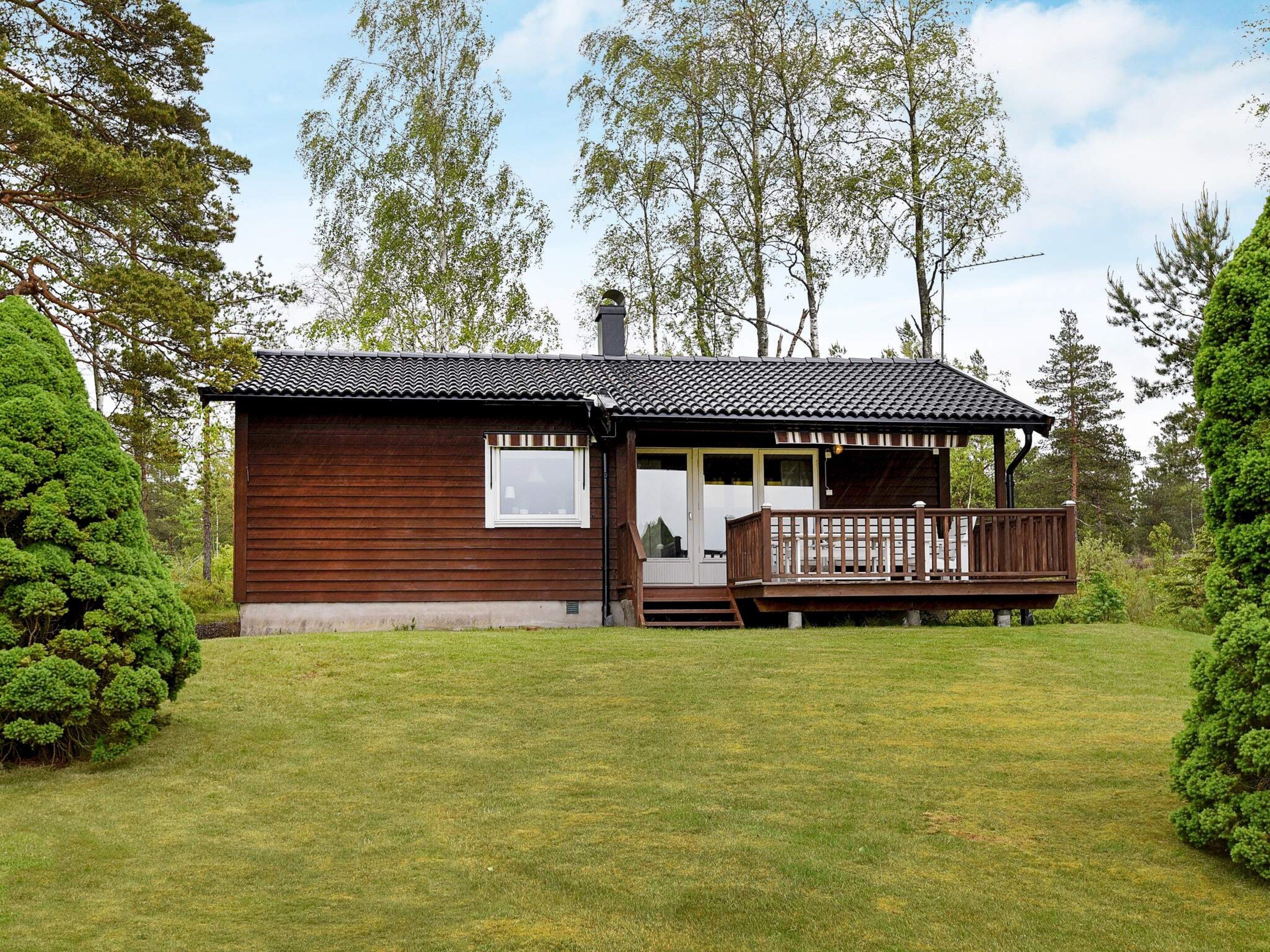 A wooden cabin with a porch and a small deck, surrounded by a well-maintained lawn and trees.