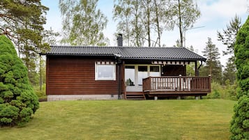 A wooden cabin with a porch and a small deck, surrounded by a well-maintained lawn and trees.