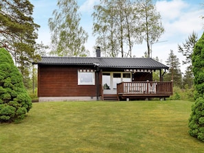 A wooden cabin with a porch and a small deck, surrounded by a well-maintained lawn and trees.