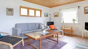 Un salon chaleureux avec un plafond en bois, un canapé gris, une table basse en bois et une fenêtre donnant sur un beau paysage.