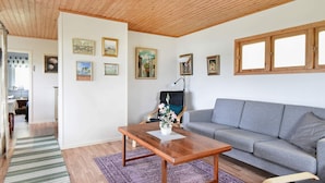 Un salon avec un plafond en bois, un canapé gris, une table basse en bois et un tapis violet.