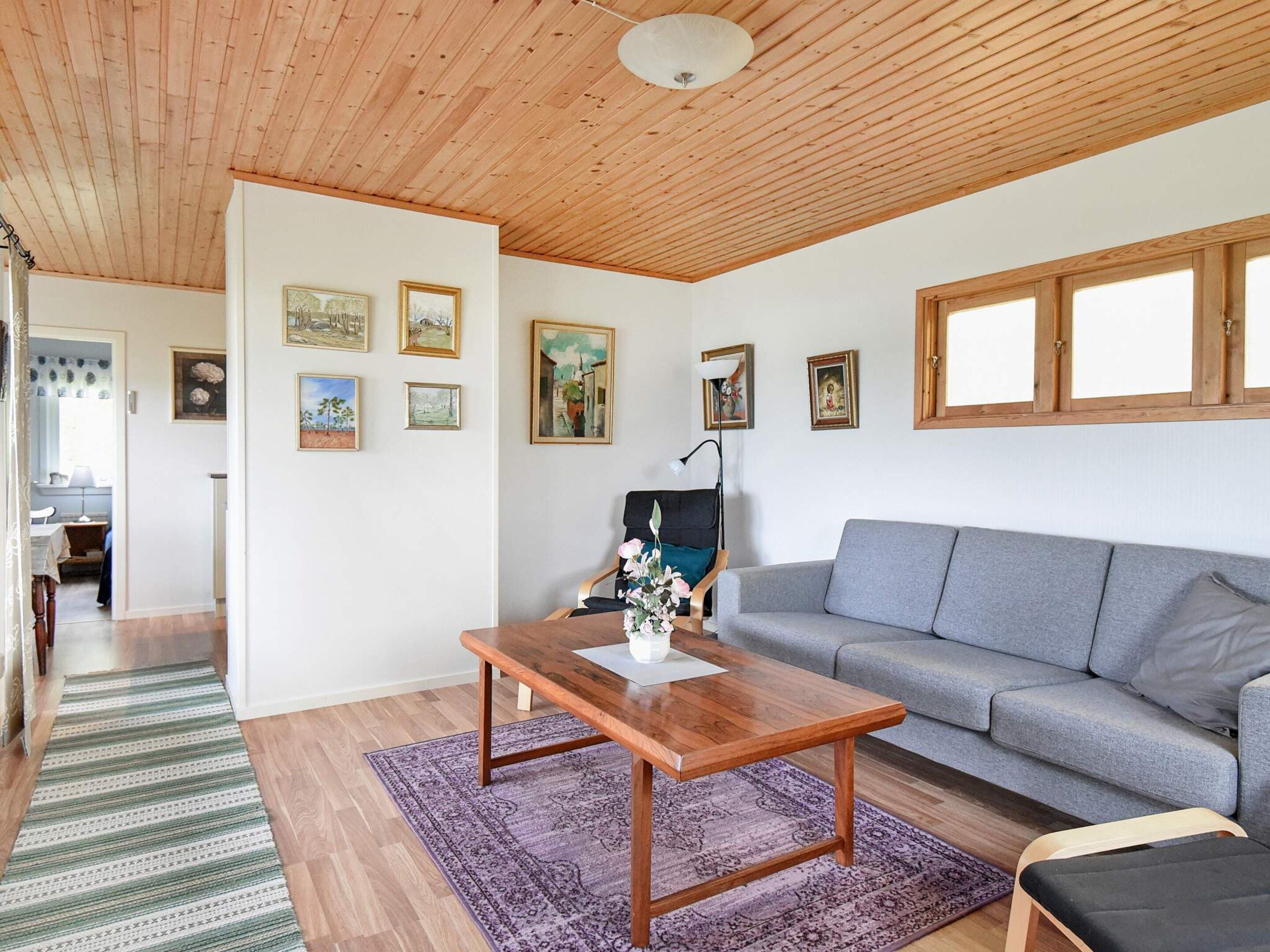 Uma sala de estar com teto de madeira, um sofá cinza, mesa de centro de madeira e tapete roxo.