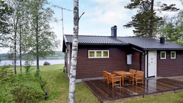 Uma cabana com varanda, mesa e cadeiras, e vista para um lago.
