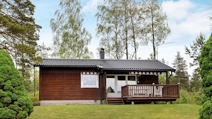 Une petite cabane en bois dotée d’un porche, entourée d’une pelouse bien entretenue et de grands arbres.