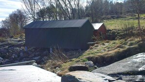 A wooden dock leading to a small building with a metal roof, surrounded by rocks and sparse vegetation.