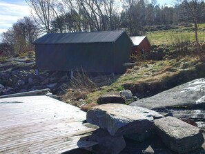 A wooden dock leading to a small building with a metal roof, surrounded by rocks and sparse vegetation. - 6 Person Holiday Home in Halsanaustan (Heim)