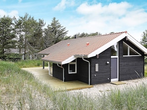A small, single-story building with a sloped roof, a wooden deck, and a sandy ground. - Quaint Holiday Home in Skagen near Sea (Skagen)