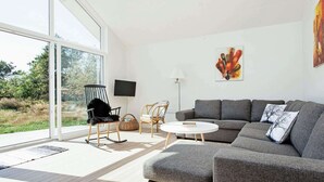A modern living room with a grey sectional sofa, a round coffee table, and two wicker chairs. A flat-screen TV is mounted on the wall, and a painting is displayed above the sofa. - 6 Person Holiday Home in Nykobing Sj-by Traum (Nykobing Sjaelland)