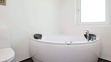 Et moderne badeværelse med et stort badekar, toilet og et vindue der giver naturligt lys.
