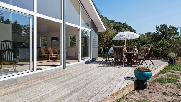 A modern house with a large glass door leading to a patio area with outdoor furniture and a potted plant. - 6 Person Holiday Home in Nykobing Sj-by Traum (Nykobing Sjaelland)