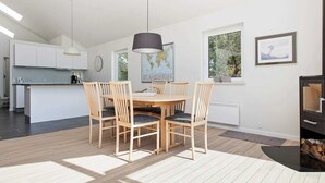 A modern kitchen with white cabinets, a dining area with a wooden table and chairs, a map on the wall, and a large window with a view of trees. - 6 Person Holiday Home in Nykobing Sj-by Traum (Nykobing Sjaelland)