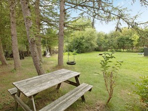 A wooden picnic table in a grassy yard with trees and a swing hanging from a tree.