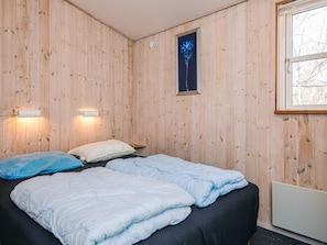 A room with wooden walls, a bed with blue bedding, two wall-mounted lights, and a window with a view of bare trees. - 4 Star Holiday Home in Ebeltoft (Ebeltoft)