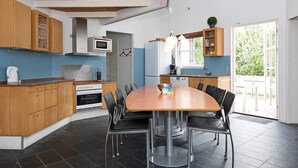 A modern kitchen with wooden cabinets, a dining table with chairs, and a large window. - 4 Star Holiday Home in Ebeltoft (Ebeltoft)