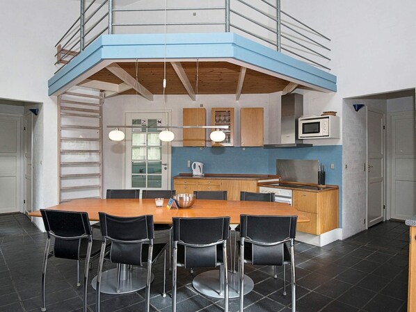A modern kitchen with a central island, black chairs, and a mezzanine level with a railing.