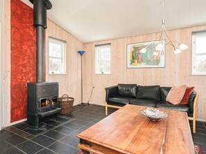 A cozy room with a black wood-burning stove, a black leather sofa, a wooden coffee table, and a painting on the wall.