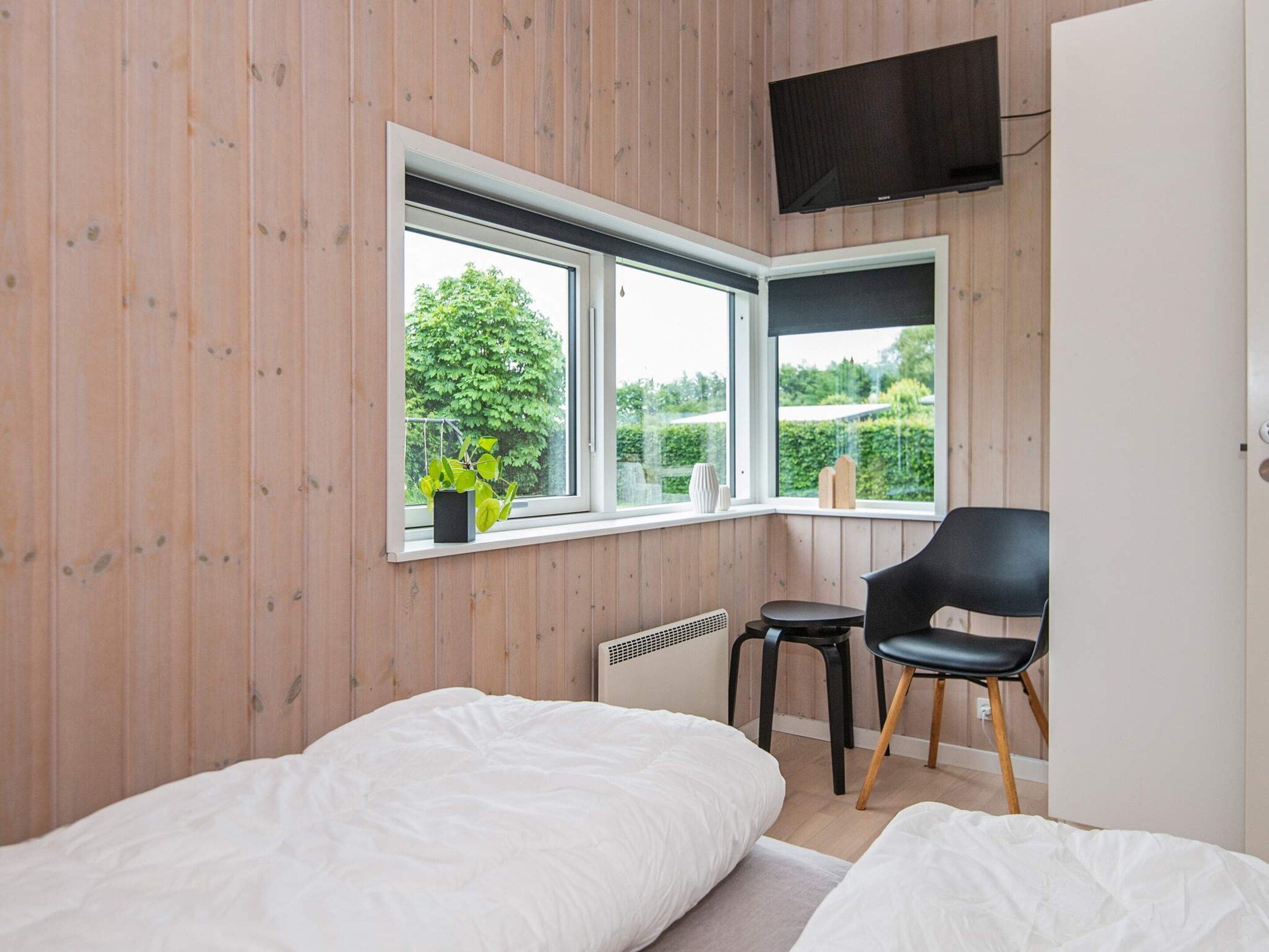 Un dormitorio con dos camas, un televisor montado en la pared, una silla y una ventana con vistas a zonas verdes.