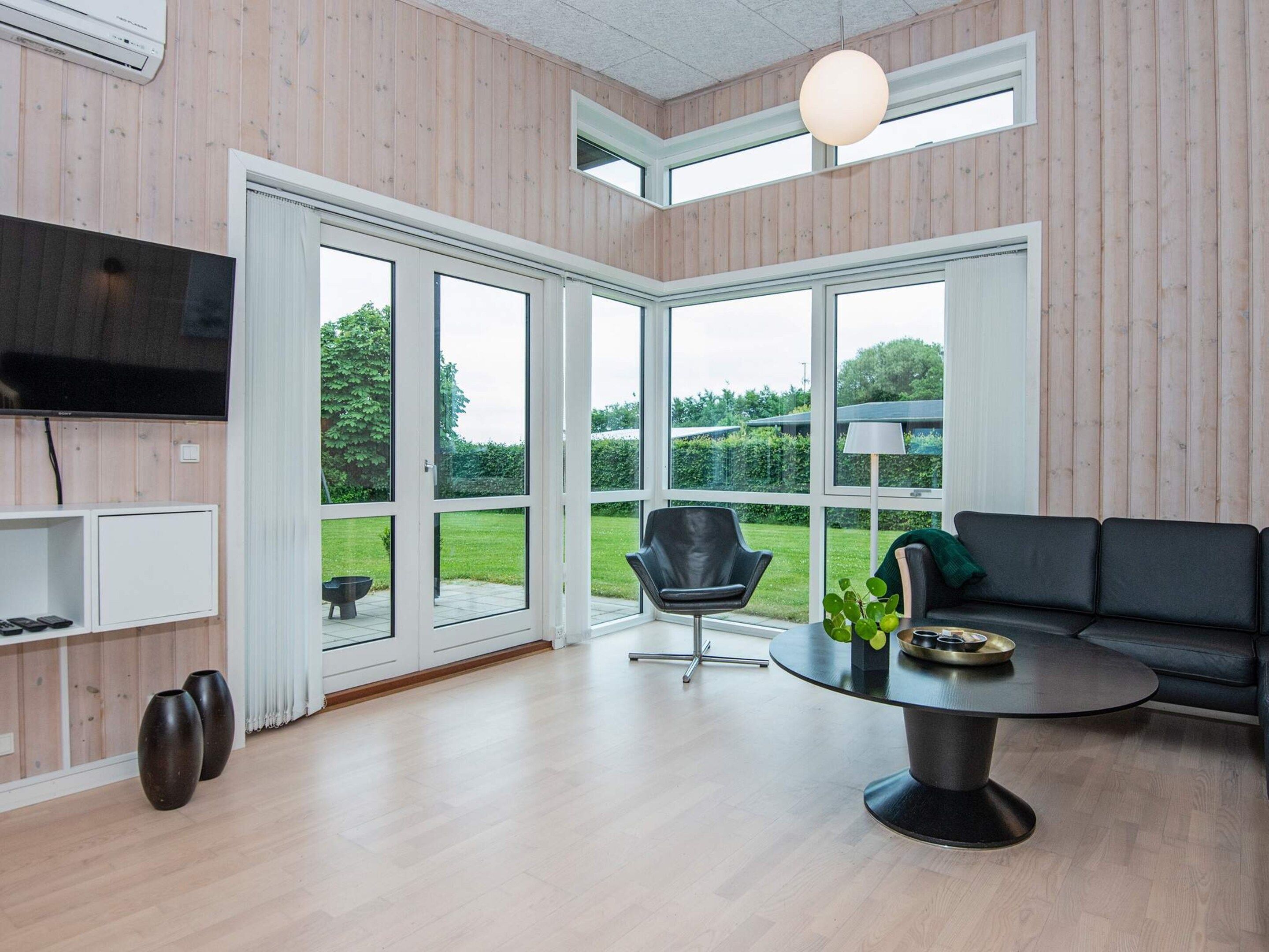 A modern living room with a flat-screen TV, a black leather chair, a round table with a lamp, and a sofa.