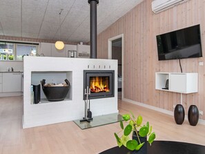 A modern living room with a fireplace, a flat-screen TV, and a kitchen area. - 5 Star Holiday Home in Haderslev (Haderslev)