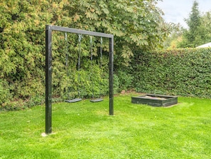 A swing set in a grassy area with a hedge and trees in the background.