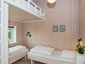 A bedroom with a loft bed, two single beds, a window, wall-mounted artwork, and a potted plant.