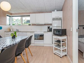 A compact kitchen with white cabinets, a microwave, a coffee maker, and a dining area with a table and chairs. - 5 Star Holiday Home in Haderslev (Haderslev)