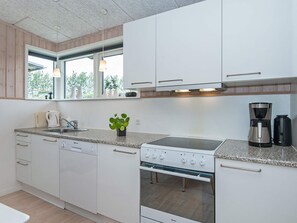 A modern kitchen with white cabinets, a built-in oven, a stovetop, and a coffee maker.
