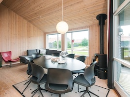 Et moderne interiør med et rundt bord omgivet af stole, en rød stol, en sofa og et stort vindue med udsigt udad.
