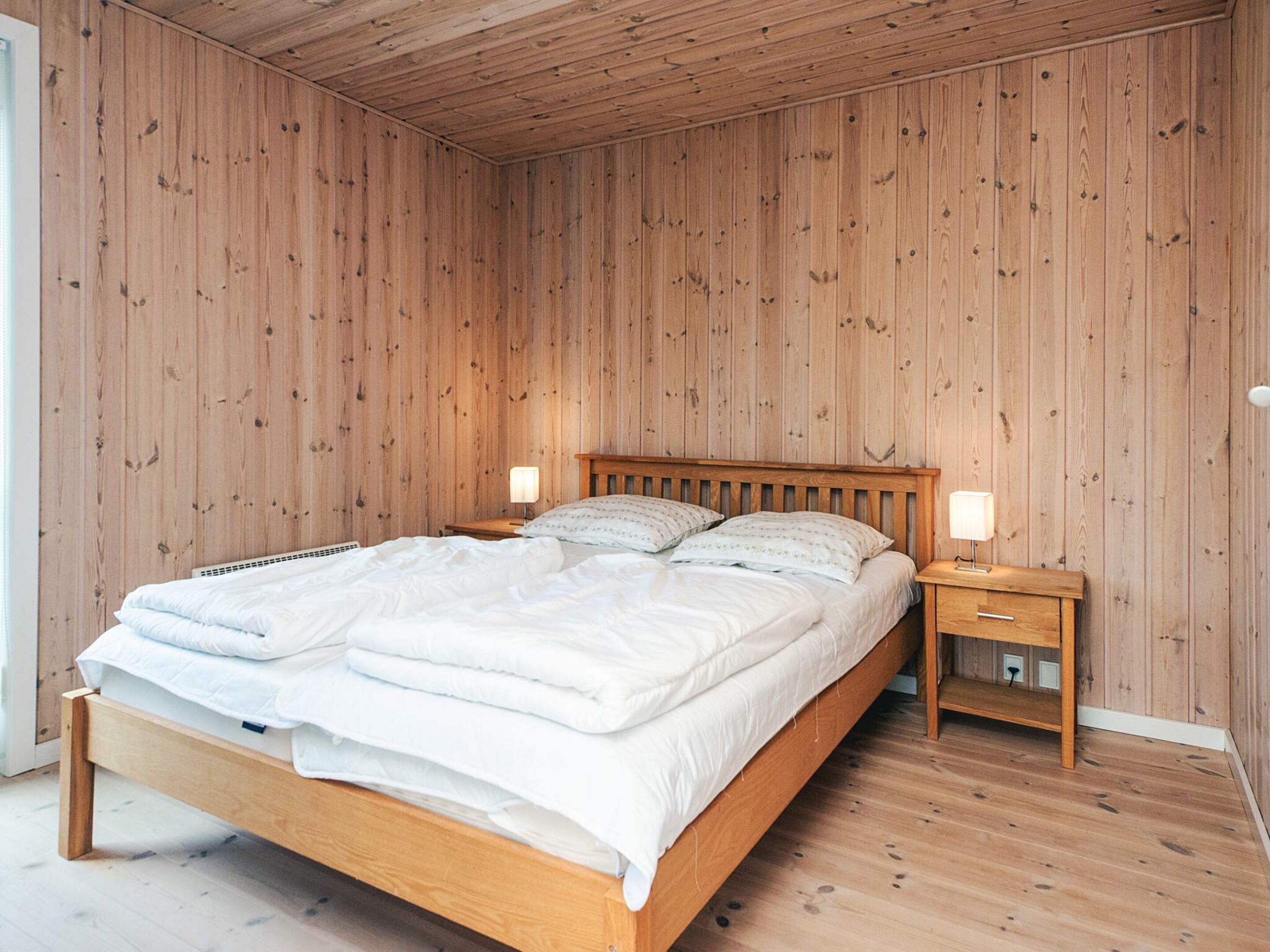 Une chambre à coucher aux murs lambrissés, avec un lit, des lampes de chevet et une table de chevet.