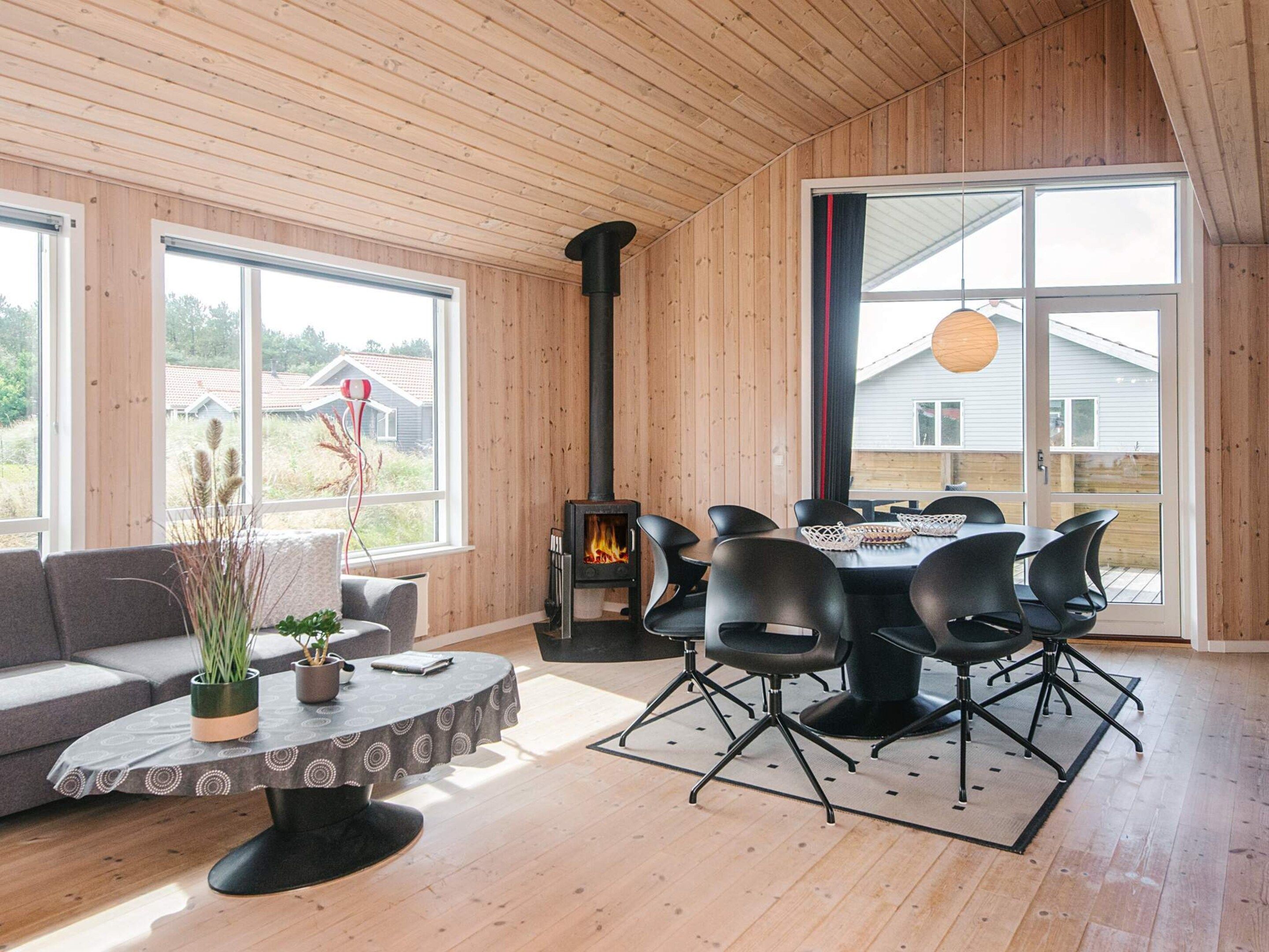 Un interior moderno con una mesa de comedor redonda, sillas negras, un sofá gris y una estufa de leña.