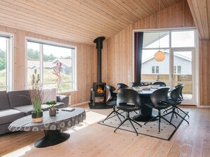 A modern interior with a wooden ceiling, a fireplace, a dining area with chairs, and large windows. - Cozy Holiday Home in Ulfborg near Sea (Ulfborg)