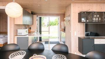 A modern kitchen with wooden cabinets, a dining area with black chairs and woven baskets, and a large window providing a view of the outdoors.