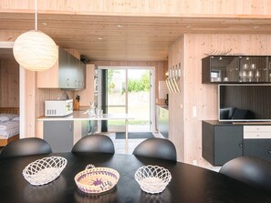 A modern kitchen with wooden cabinets, a dining area with black chairs and woven baskets, and a large window providing a view of the outdoors. - Cozy Holiday Home in Ulfborg near Sea (Ulfborg)