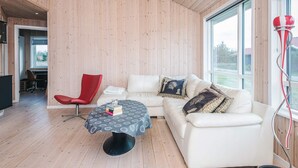 Una sala de estar moderna con un sofá blanco, un sillón rojo y una mesa redonda con mantel estampado.