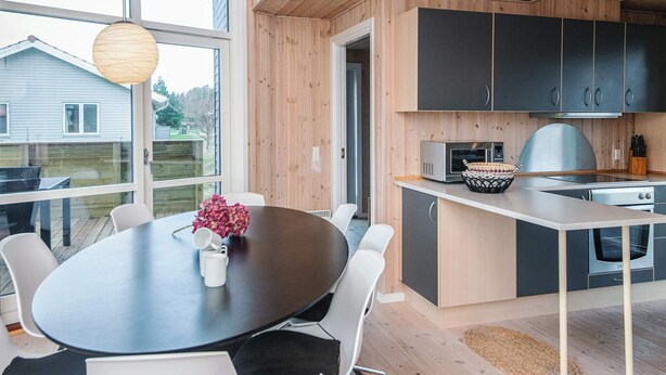 Una cocina moderna con armarios oscuros, una isla central y una zona de comedor con una mesa redonda y sillas.