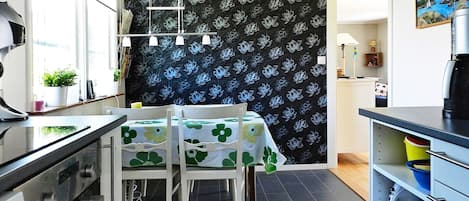 A modern kitchen with a dining area, featuring a black floral wallpaper, a coffee machine, and a small plant on the counter.