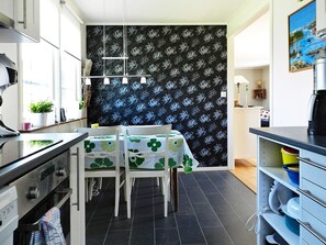 A modern kitchen with a dining area, featuring a black floral wallpaper, a coffee machine, and a small plant on the counter. - Holiday Home in Lysekil (Lysekil)