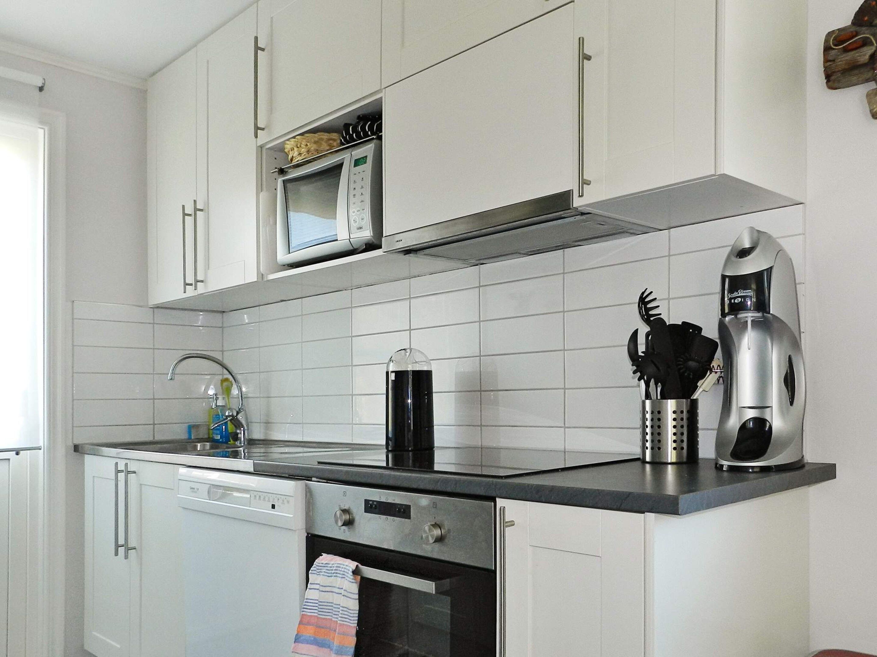 Una cocina con gabinetes blancos, microondas, cafetera y lavavajillas.