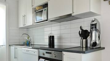 Una cocina con gabinetes blancos, microondas, cafetera y lavavajillas.