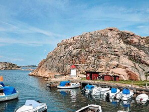 A rocky coastline with boats docked at a pier, a lighthouse, and a small red building. - Holiday Home in Lysekil (Lysekil)